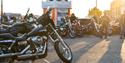 Old black bike parked up with riders admiring in the background