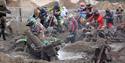 Riders and motorbikes, some abandoned, stuck in deep mud during a beach motorbike race