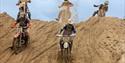 A group of five motorbike riders coming down a large sand dune