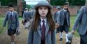 Matilda in a grey hat and school uniform walking through school gates with other children