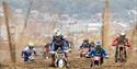 Sand sprays up high behind a group of motorbike racers in a beach race