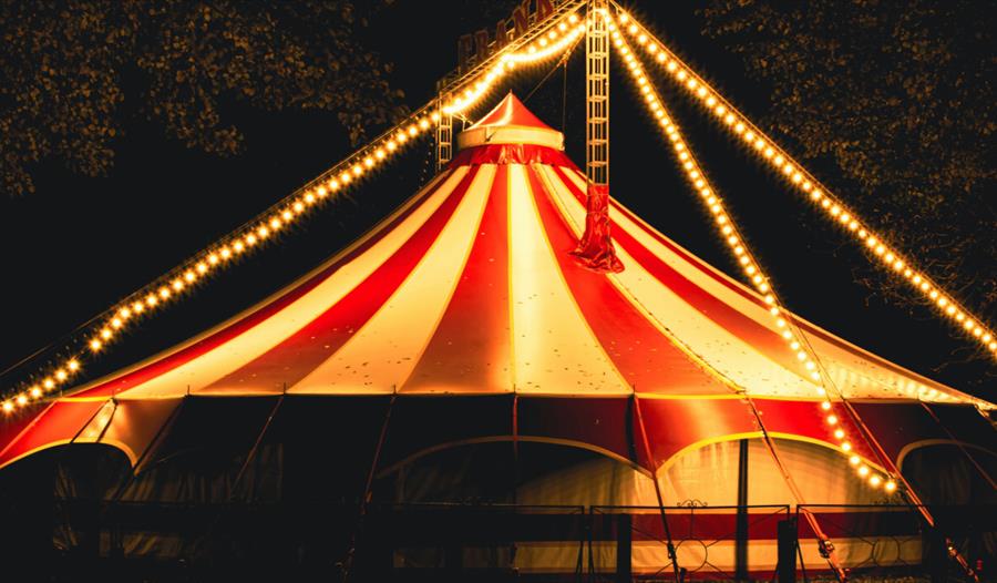 Red and white circus tent draped with neon yellow string lights