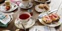 A serving of Afternoon Tea for two. There are three china plates, one with a cake and strawberry, one with a scone cut in half spread with clotted cre
