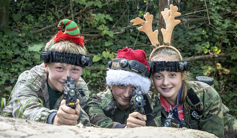 Children wearing camouflage clothing with Christmas hairbands on and holding toy guns.