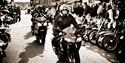 Black and white photography of mounted motorcyclist surrounded by motorcycles.