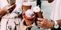 Crop unrecognizable friends clinking ice creams on street
