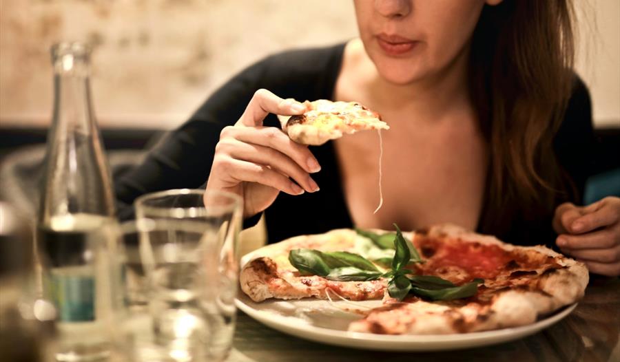 Woman Holds Sliced Pizza Seats by Table With Glass