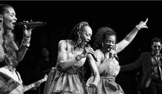 Boney M consisting of 4 members on a stage singing. The photo is in black and white.