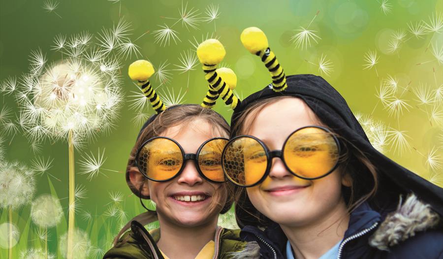 Two girls wearing bee headbands in front of a green background.