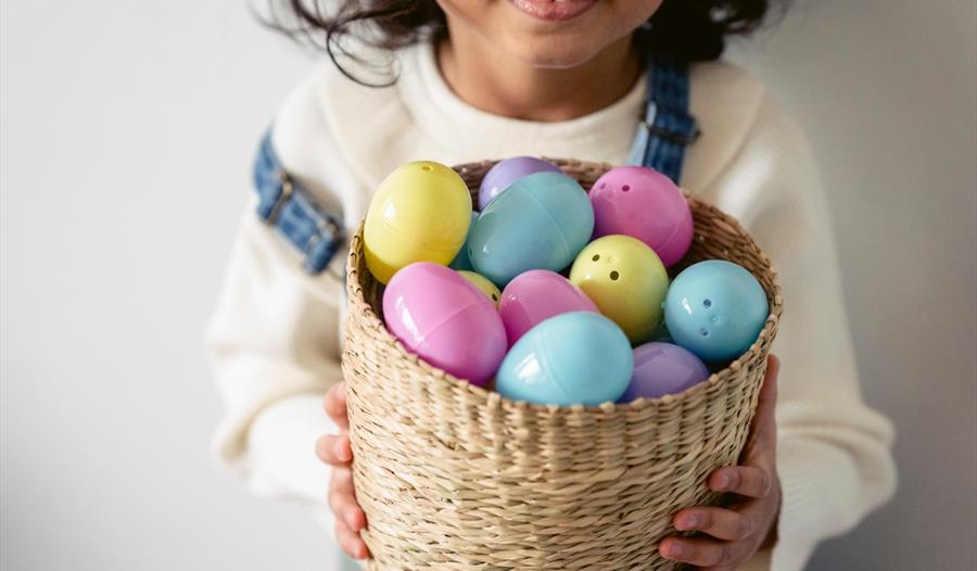 Girl in White Crew Neck Shirt Holding Brown Woven Basket With Assorted Color Easter Eggs