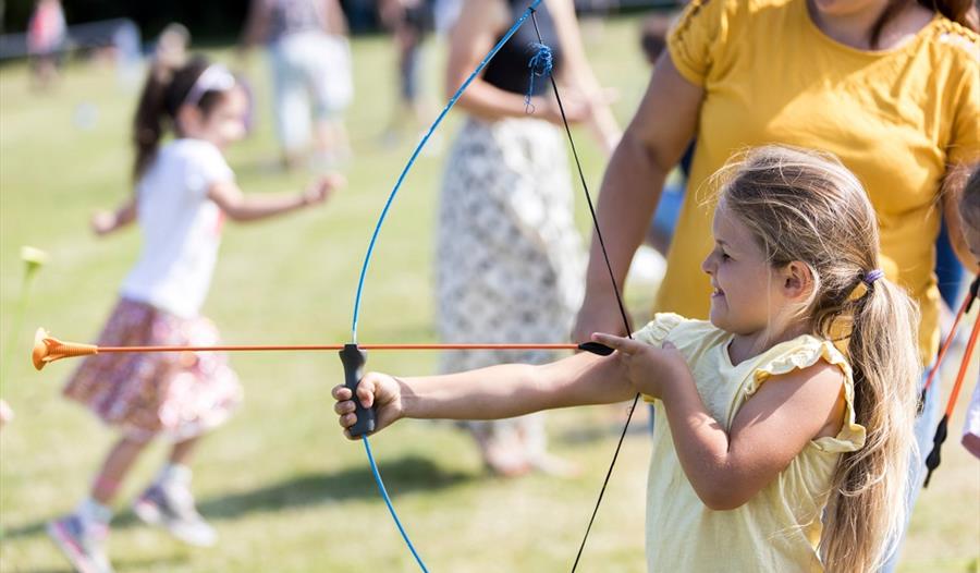 Image shows a young girl practicing archery as an adult looks on