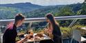 A couple eating lunch on a balcony with a scenic view.