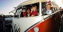Father and children smiling at the camera in their red VW campervan