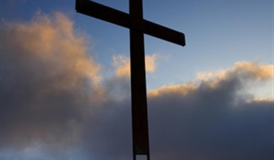 A giant cross stands against a blue, cloud-filled sky.
