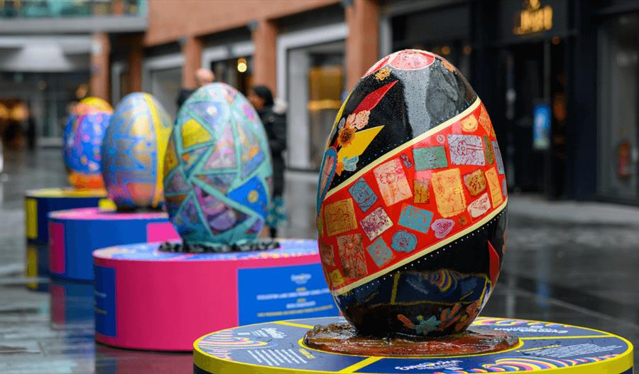 A row of giant, colourful and shiny painted eggs, lined up next to each other inside the shopping mall Liverpool ONE