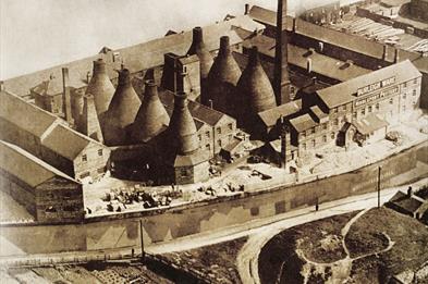 Image of a built-up pot bank pre 1950s. It is sepia toned and mix of bottle kilns and buildings 