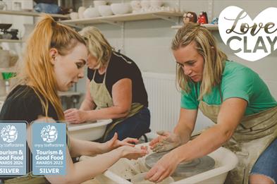 Two ladies throwing a pot at LoveClay Ceramics Centre, infront of them is a studio instructor helping one of the ladies.