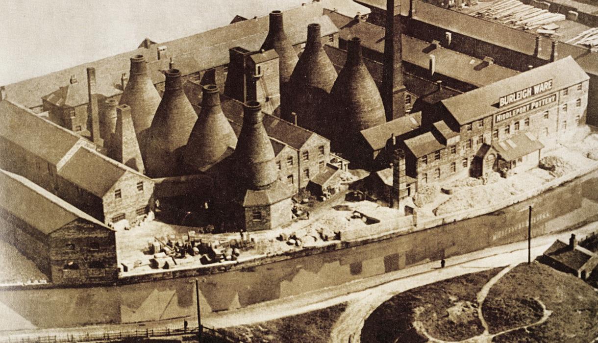 Image of a built-up pot bank pre 1950s. It is sepia toned and mix of bottle kilns and buildings