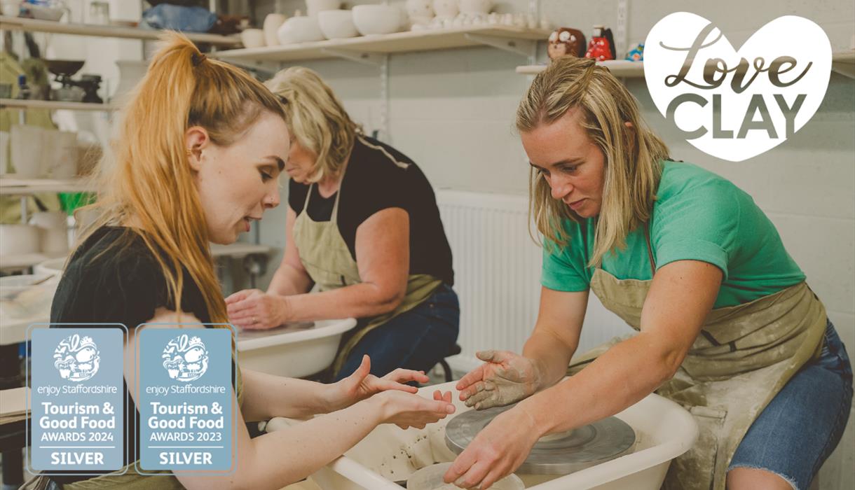 Two ladies throwing a pot at LoveClay Ceramics Centre, infront of them is a studio instructor helping one of the ladies.