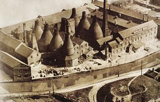 Image of a built-up pot bank pre 1950s. It is sepia toned and mix of bottle kilns and buildings