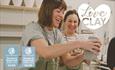Image shows two visitors laughing as one moulds a slab of clay
