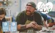 A visitor, with tattooed arms, a ginger beard, glasses and a cap the wrong way around, smiles at his friend