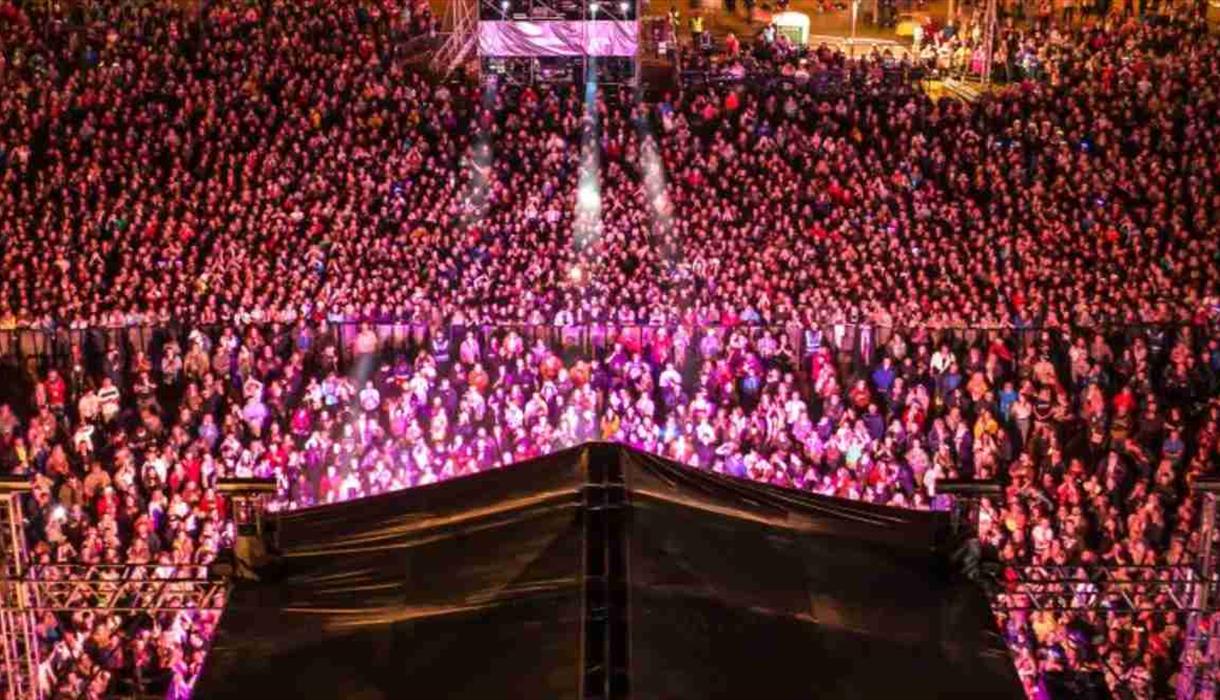 Image shows a stage from above and a crowd of thousands enjoying the performance