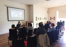A woman lecturing in front of a presentation on a large screen