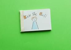 A small book with the title kick the ball and a drawing of a child in a blue top