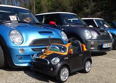 Four Mini brand cars lined up next to eatch other with a smaller Mini for children in front of them.