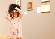 A child dressing up in a large hat in front of an artwork