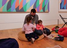 Children playing with adult under Bridget Riley Painting