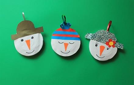 Three snowman heads made from paper and recycled plastic with ribbons for hanging