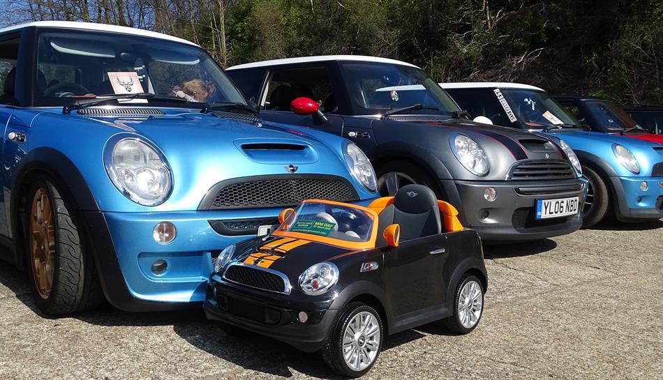 Four Mini brand cars lined up next to eatch other with a smaller Mini for children in front of them.