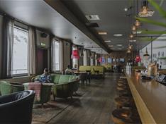 A reception desk and lounge with a guest seated in a couch in the foreground, with restaurant tables and two guests seated at a table in the backgroun