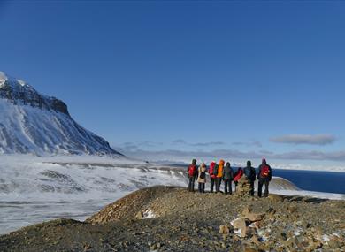 People on a small mountain looking out in the nature with snowcovered grounds and mountain in the background
