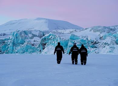 Three people walking in front of a blue glacier.