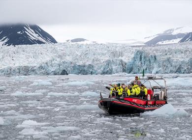 Several people in open RIB boat in front of glacier. The fjord is full of ice. 
