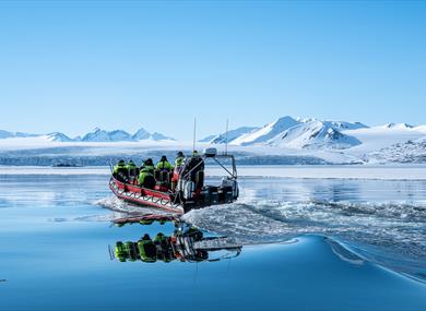 An open RIBboat travels through Arctic waters surrounded by snow-covered mountains.
