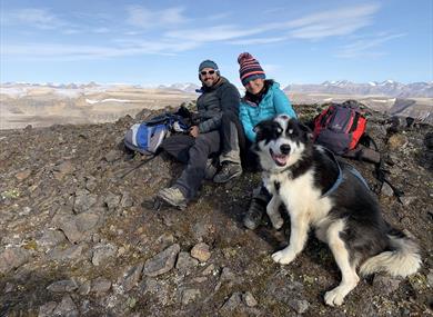 Two persons and a dog relaxing on top of a mountain