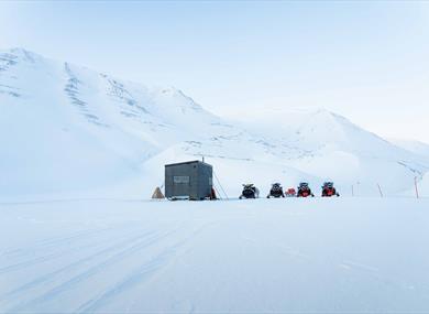 Snowmobiles parked next to a wilderness cabin 