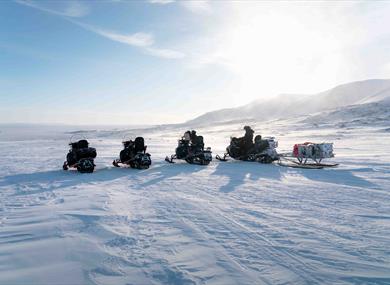 Four snowmobiles are parked on one row, in a white and snowcovered landscape 