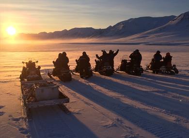 A tour group on snowmobiles looking towards the sun