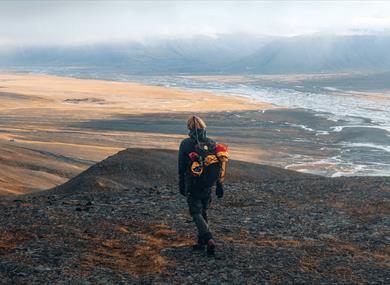 Person hiking in the mountains during the summer, facing a wide valley. 