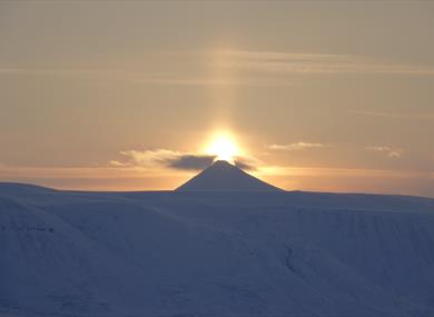 The midnight sun shining behind a mountain peak