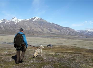 Person hiking with dog towards a cabin