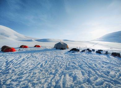 A winter landscape with tents set up on the snow under a clear sky.