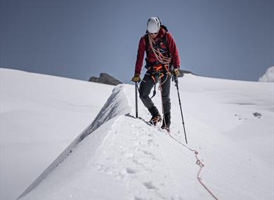 A person with glacier safety equipment hiking on a glacier