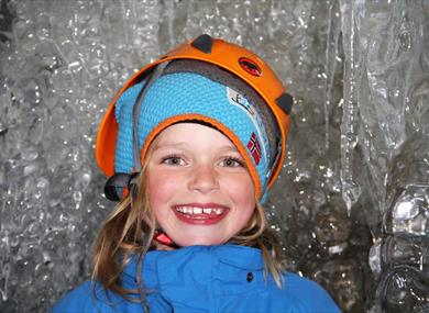 Happy and smiling kid, wearing a helmet inside the icecave  