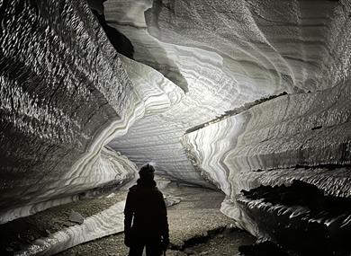 Person standing inside an ice cave with a head lamp